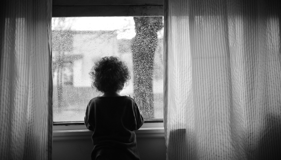 Un bambino che guarda fuori dalla finestra mentre piove